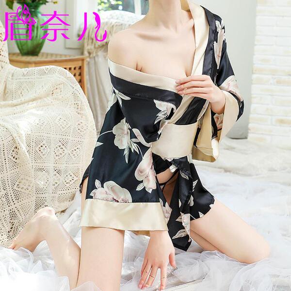 A woman wearing a black floral print robe with beige accents, tied at the waist, sitting on a white surface. the design featu...