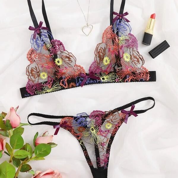Vibrant floral embroidered lace bra and panty set with purple bows, styled with roses, lipstick, and a heart necklace.