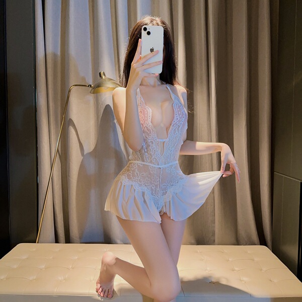 Woman wearing white lace bodysuit with tie-neck and open-crotch design, posing on bed in soft lighting.