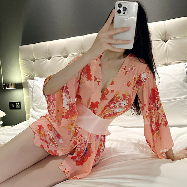 A woman poses on a bed wearing a peach-colored sheer japanese-style kimono sleepwear set from 2025. the outfit features flora...