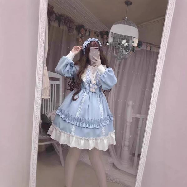 A woman poses in a mirror wearing a light blue 2026 cute sweet lolita dress, featuring long sleeves, ruffled layers, and flor...