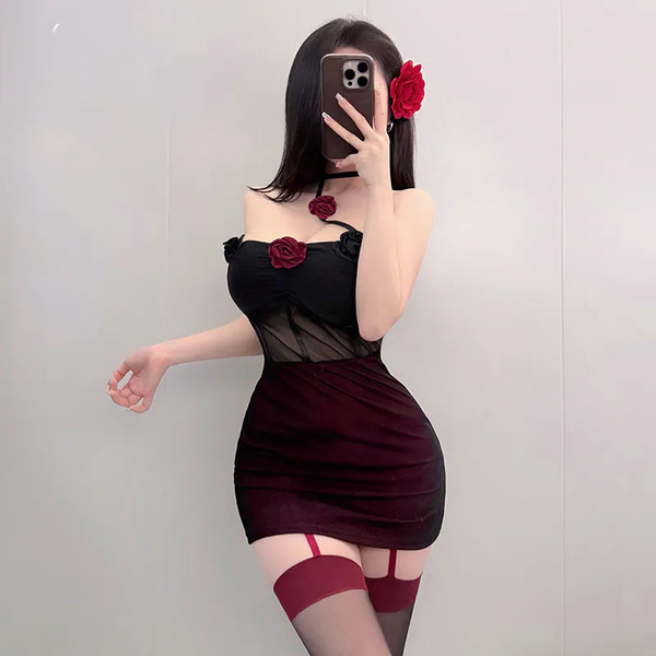 A woman poses in a black sheer slip dress adorned with red roses, paired with thigh-high stockings featuring garter straps, c...