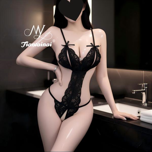 Woman wearing a sexy black lace bodysuit with sheer cut-outs and bow details, posing in a modern bathroom setting.