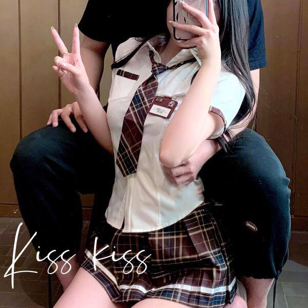 A person wearing a schoolgirl uniform with a plaid skirt and tie, posing playfully while holding a phone. the outfit features...