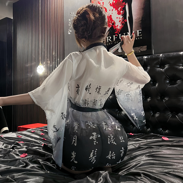 A woman sits on a bed wearing a muroa japanese kimono sleepwear set, featuring a white robe with black ink-inspired poetry pr...