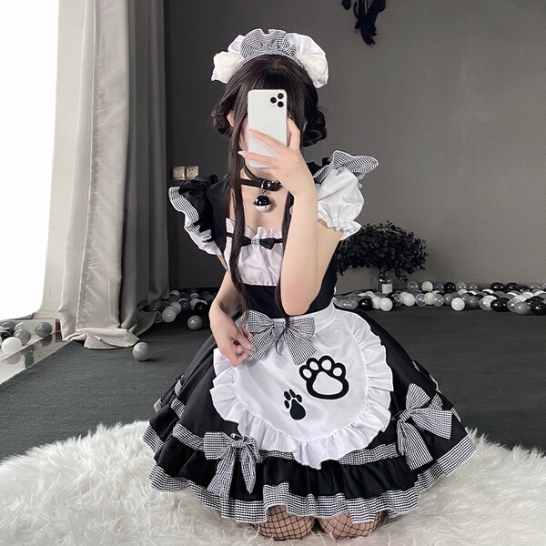 A person wearing a black and white maid costume with paw prints, taking a mirror selfie. the outfit features ruffles and bows...