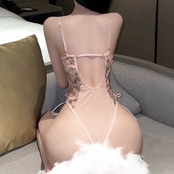 Woman wearing a pink cherry blossom lace bodysuit with heavy embroidery and a deep v plunge back, featuring delicate mesh cam...