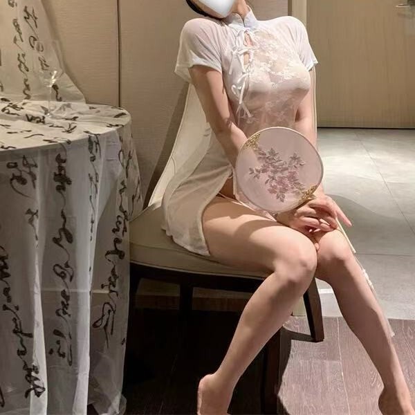 A woman sits elegantly wearing a sheer cherry blossom lace qipao sleepwear set, featuring vintage-inspired design elements an...