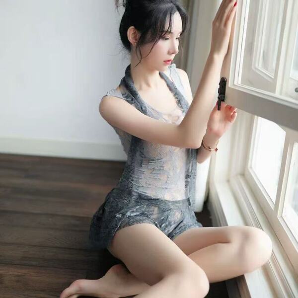 Woman in cherry passion lingerie set, sheer nightwear with thong, sitting by window.