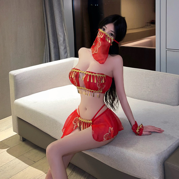 A woman poses on a couch wearing a vibrant red chinese new year-themed lingerie set. the outfit features intricate designs in...