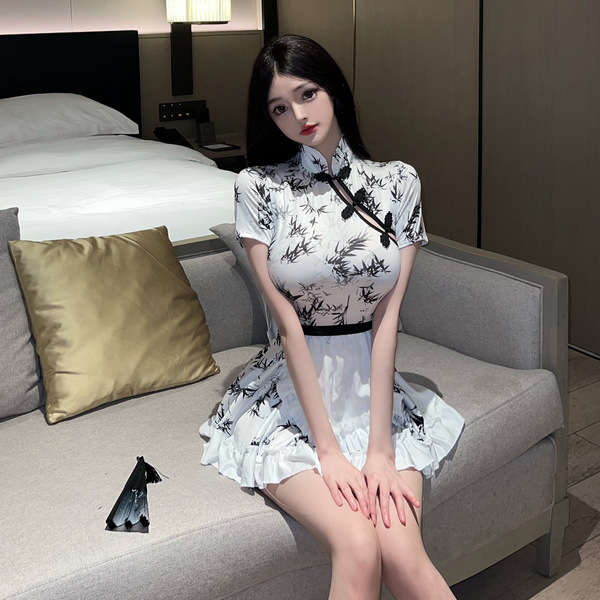 A woman sits on a couch wearing a white chinese new year-themed dress inspired by a qipao, featuring black floral patterns an...