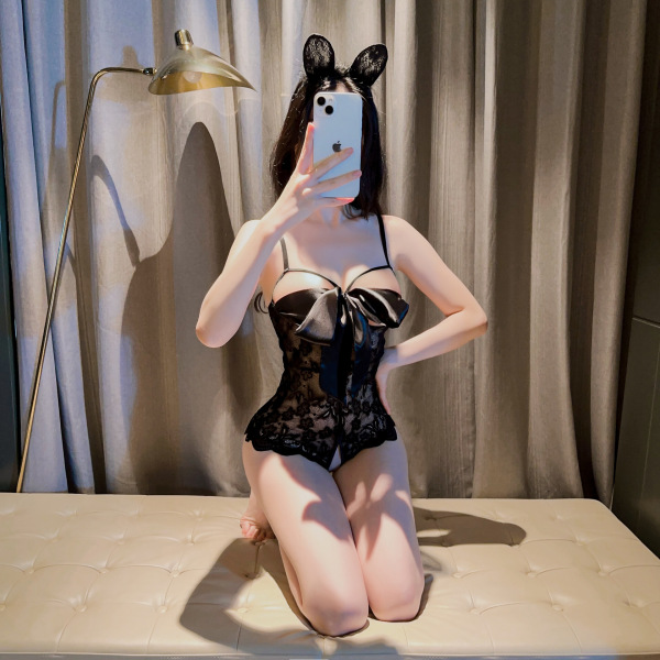 Woman wearing black lace lingerie set with bow, posing on bed in romantic nightwear outfit for couples.