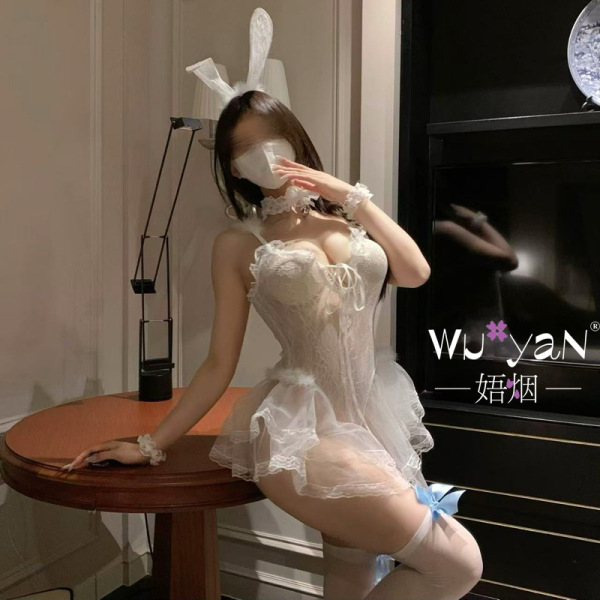 Woman in white lace bunny girl lingerie with ears, garters, and playful jk-style details, posing seductively indoors.
