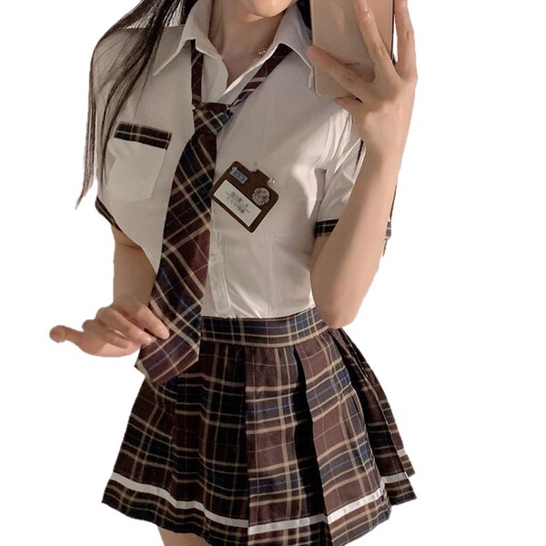 A person wearing a schoolgirl uniform with a white blouse, plaid skirt, and tie, holding a phone to take a selfie.
