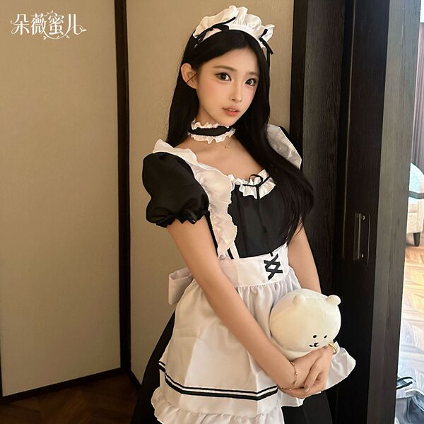 A woman wearing a black and white maid costume holding a plush bear, suitable for cosplay and role play.