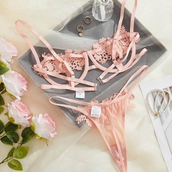 Pink lace lingerie set with floral details, styled on a tray with roses and jewelry.