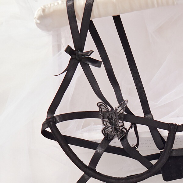 Black sheer lingerie set with lace butterfly detail and adjustable straps, styled on a white chair for bold, sensual elegance...
