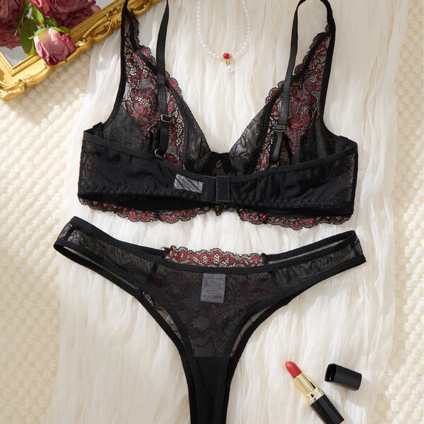 Black lace bra and panty set with red floral details, displayed on white fur with lipstick and pearls.