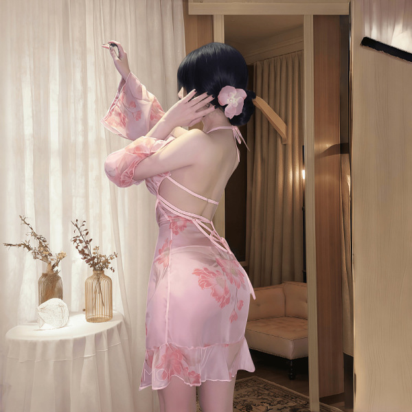 Woman wearing pink floral backless chemise with sheer fabric and side slit, styled as sensual sleepwear in soft-lit bedroom s...