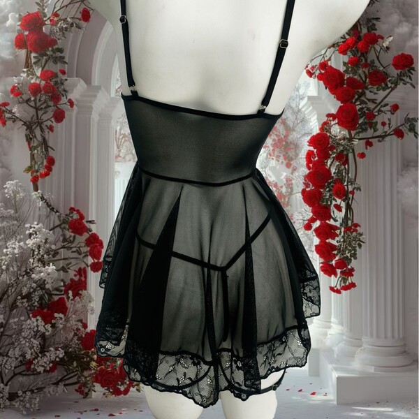 Black sheer chemise nightgown with lace trim and backless design, paired with matching thong, displayed on mannequin amidst r...
