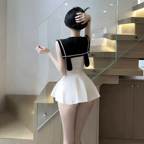 Woman wearing a cute sailor-style jk uniform set with a white skirt and black top, posing indoors near a staircase.