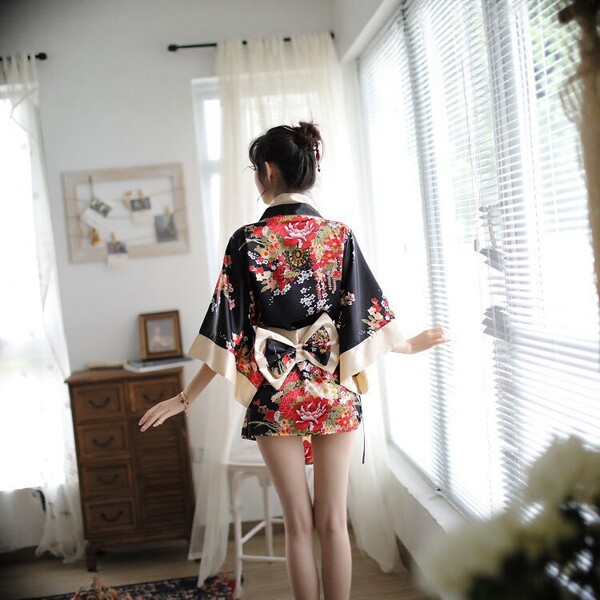 A woman stands by a window wearing a japanese kimono-style lingerie set, featuring vibrant floral patterns and a bow tie, per...
