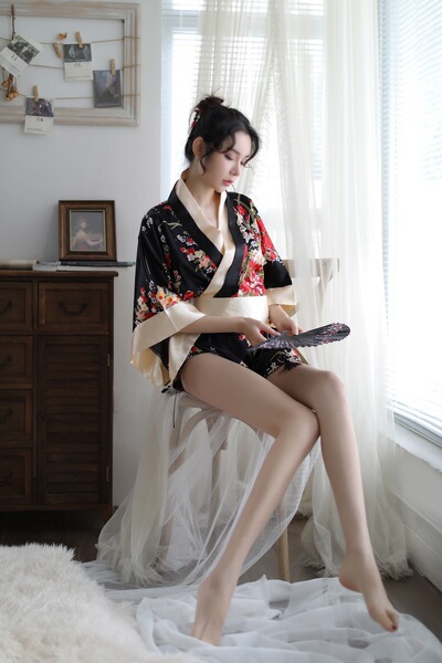 A woman sits gracefully by a window wearing a black floral japanese kimono, holding a fan. the elegant design features intric...