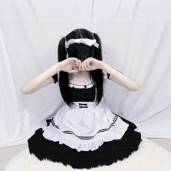 A woman wearing a japanese maid cosplay dress, featuring black and white colors with ruffles, sitting against a white backdro...