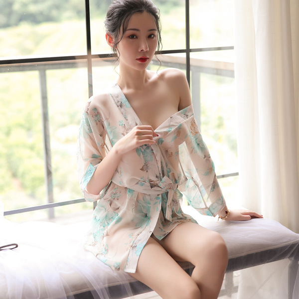A woman sits by a window wearing a sheer lace sleepwear set, featuring a delicate floral pattern. the outfit includes a tie-f...