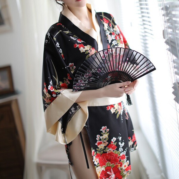 A woman wears a black japanese-style kimono with vibrant floral patterns, holding a traditional folding fan. the design featu...