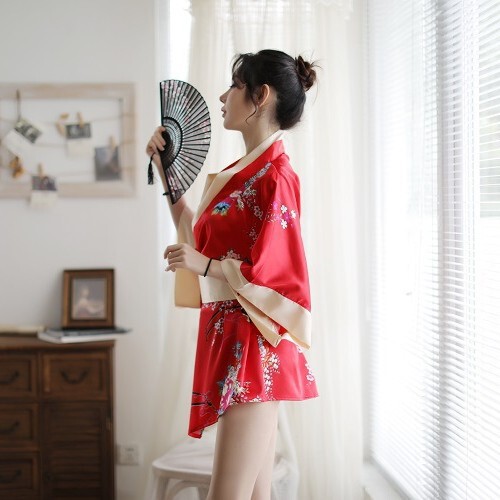 A woman stands by a window wearing a red japanese-style kimono with floral patterns and a bow design, holding a traditional f...