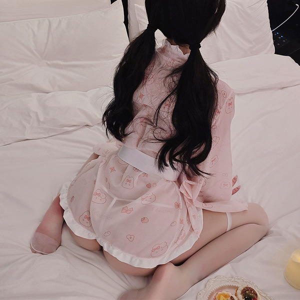 A person sits on a bed wearing a pink japanese-style sleepwear set featuring cute bunny and maid details, creating a playful ...