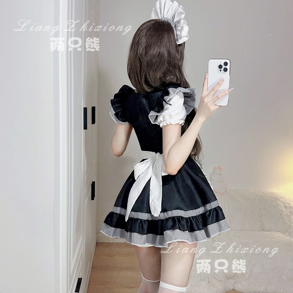 A woman wearing a black and white maid dress with puffy sleeves and a bow, taking a selfie in a room. the outfit features ruf...