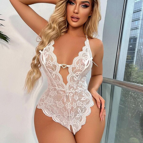 Woman wearing white lace sheer open-crotch bodysuit, sexy sleepwear with floral embroidery and heart detail.