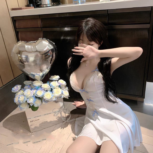 Woman in white lace-trimmed babydoll nightgown, posing beside heart balloon and blue-white roses.