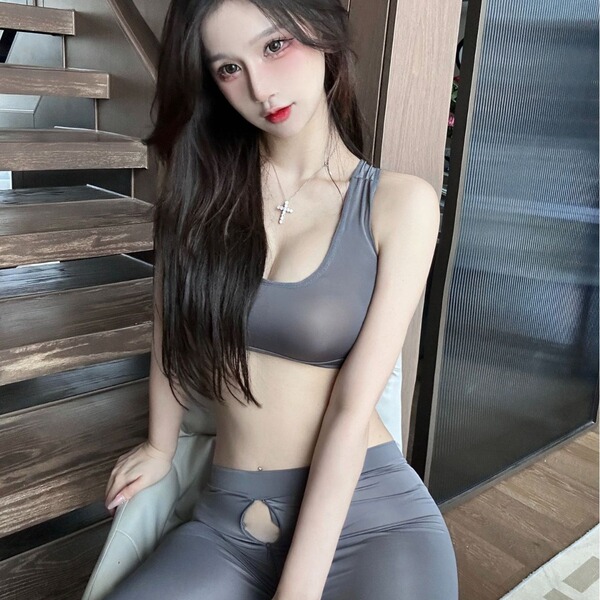 Woman wearing gray lairuru open-crotch yoga pants and matching sports bra, posing on stairs in sexy sporty lingerie outfit.