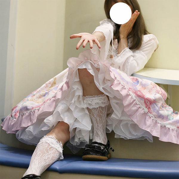 A person wearing a lolita-style dress featuring a voluminous crinoline petticoat, lace stockings, and black shoes, sitting ca...