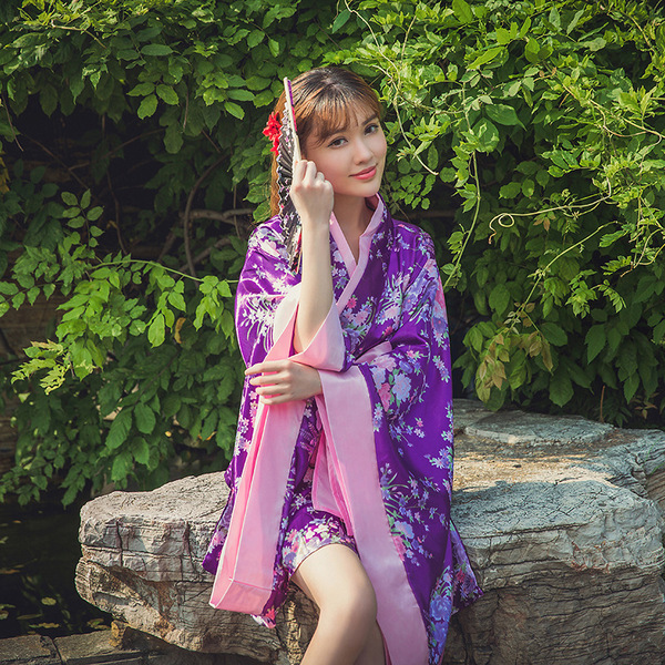 A woman wearing a purple lolita dress with cherry blossom patterns, paired with a pink obi sash, sitting gracefully on a rock...