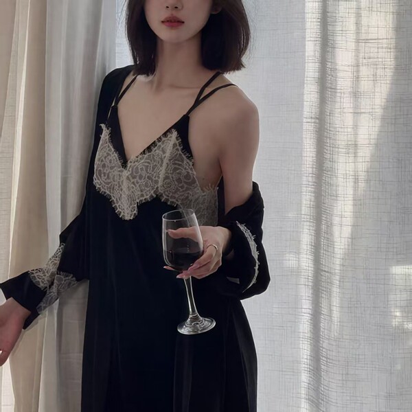 A woman wears a black lace gold velvet embroidered long sleep dress with backless design and tie belt robe set, holding a win...