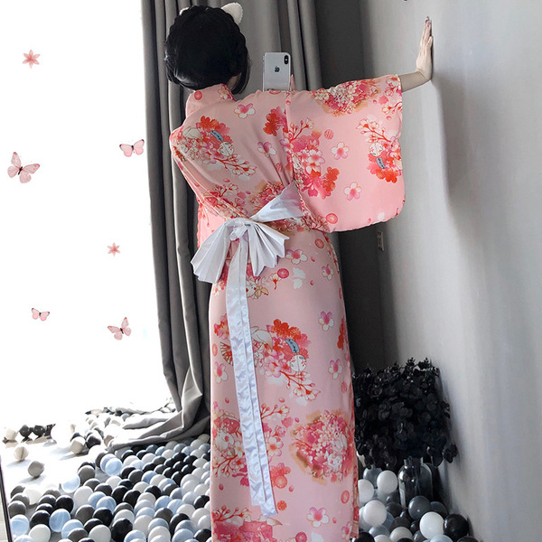 A woman stands against a wall wearing a pink floral japanese kimono-style cat-themed sleepwear set, featuring long sheer fabr...