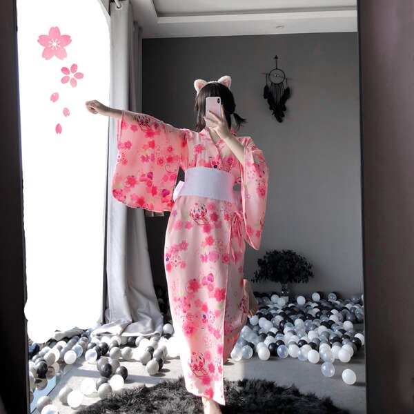 A person wearing a pink floral japanese-style kimono with cat ears takes a photo in front of a mirror, surrounded by floating...