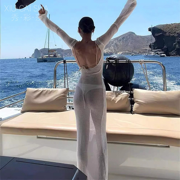 A woman stands on a boat wearing a sheer, long-sleeve beach dress with a sexy backless design, perfect for summer vacations.
