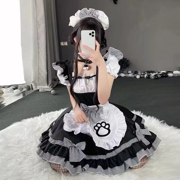 A woman wearing a black and white maid cosplay dress with ruffles, bows, and a cat paw design, sitting on a fluffy rug indoor...