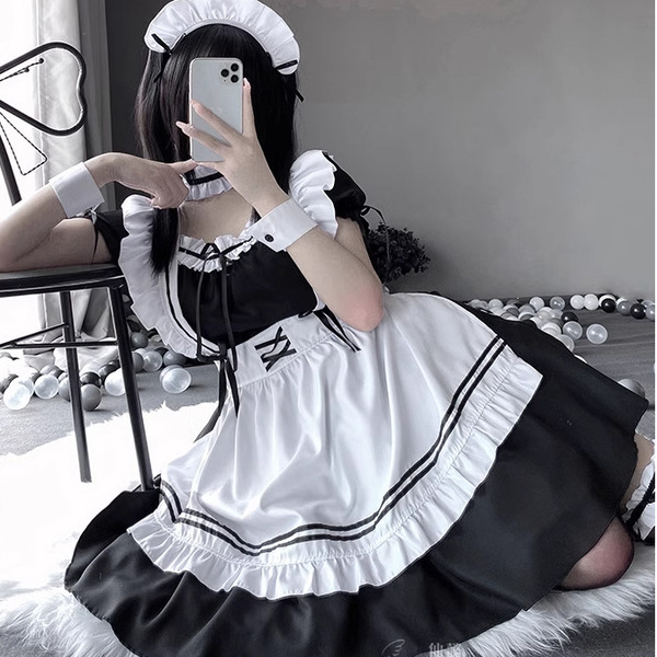 A woman poses wearing a maid costume cosplay dress, featuring black and white colors with ruffles and a sailor-style collar. ...