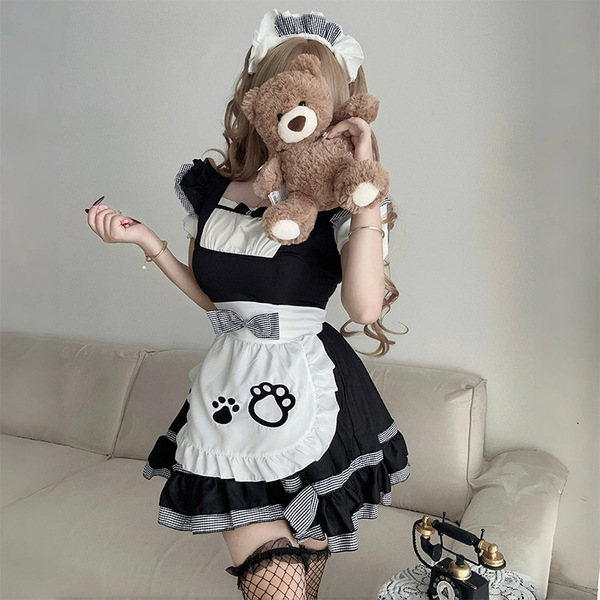 A woman wearing a black and white maid costume cosplay dress, featuring a ruffled apron with paw prints, holding a teddy bear...