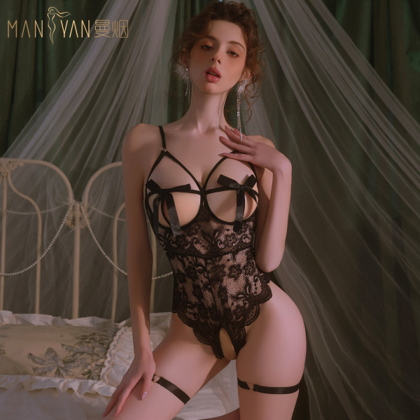 Woman wearing mannyan black lace bodysuit with bow detail and garters, posing on bed with sheer canopy background.