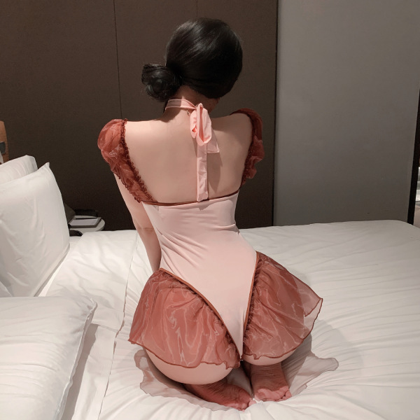 Woman in pink meimei flirty lingerie set, open-crotch bodysuit with ruffled sleeves and bow back, kneeling on bed.