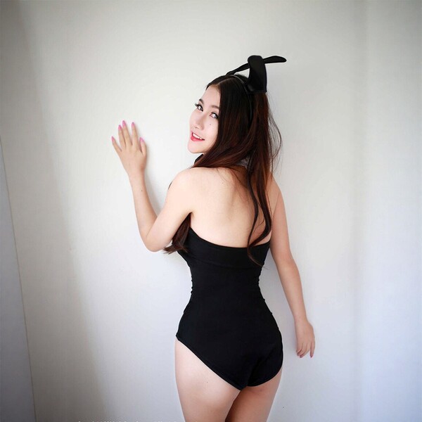 Woman in black bunny girl bodysuit with ears, posing against white wall. midnight temptation sexy deep v costume set for adul...