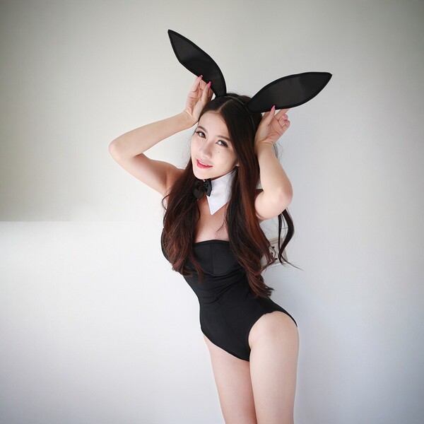 Woman wearing black midnight temptation bunny girl bodysuit with deep v neckline, bunny ears headband, and white collar.