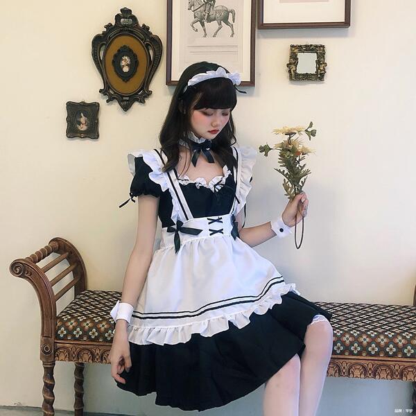 A person wearing a black and white lolita maid dress with ruffles, sitting on a bench holding flowers, styled for cosplay and...